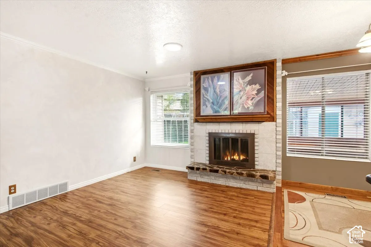 Wood-finish flooring, fireplace with a stacked-stone hearth, white-washed brick fireplace surround, wood-framed built-in shelving, and horizontal window blinds