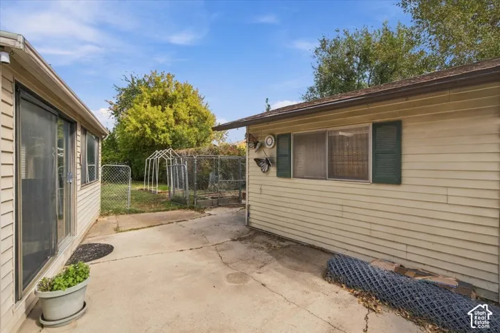 Exterior area featuring horizontal siding, a concrete patio, sliding glass door, and metal frame chain-link fencing