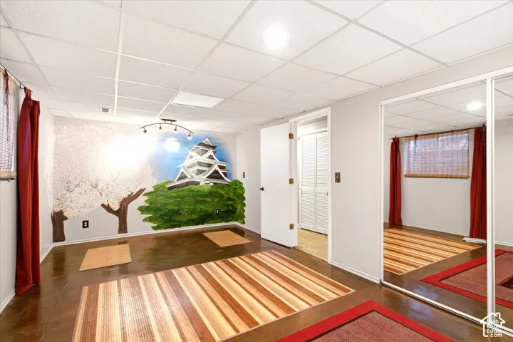 Interior space featuring stained concrete flooring, recessed lighting, drop ceiling, wall mural, and floor-to-ceiling mirrored closet doors
