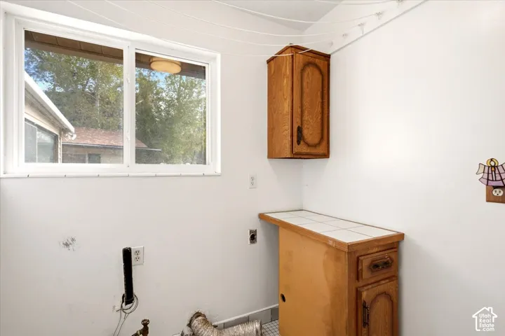 Utility area featuring a sliding window, tile-top cabinetry, wall-mounted wood-finish storage, and an installed overhead drying rack