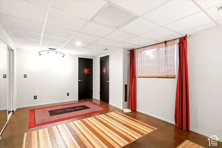 Finished interior space featuring a drop ceiling, stained concrete flooring, mirrored sliding closet doors, and multi-bulb track lighting