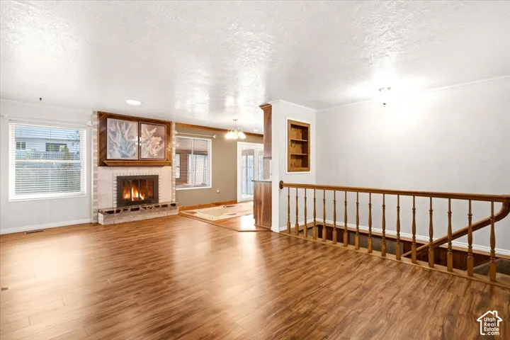 Open-concept living space featuring wood-finish flooring, a fireplace with stone-surround hearth, built-in wall niche, and wooden staircase railing
