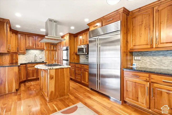 Kitchen featuring custom natural wood cabinetry, stainless steel professional-grade appliances, a central island with a gas cooktop, stone countertops, and recessed ceiling lighting