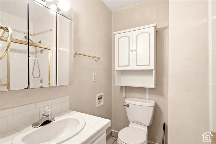 Bathroom featuring a ceramic tile countertop with an integrated basin, metal-framed mirrored medicine cabinet, built-in wall cabinetry, and a shower enclosure with gold-tone hardware