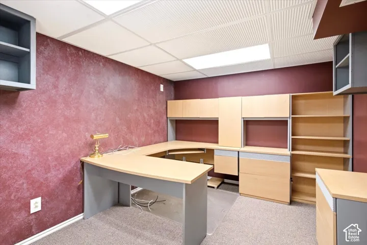 Built-in light wood cabinetry with integrated desk surface, overhead shelving, and wall-mounted storage units featuring textured maroon walls and a drop-tile ceiling