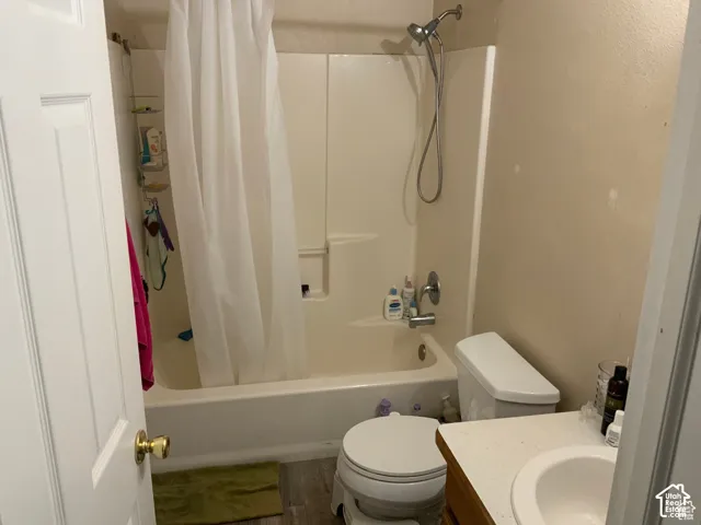 Full bathroom featuring a tub-shower combination with an integrated surround, handheld showerhead, vanity with a light-toned countertop, and wood-finish flooring