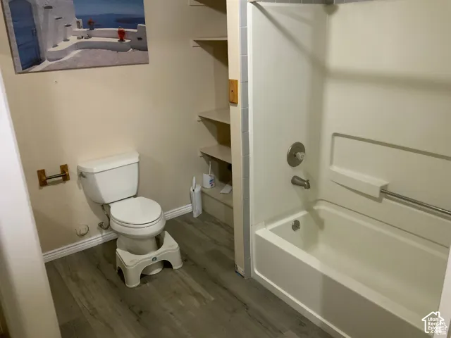 Full bathroom featuring a tub-shower combination with a surround, wood-finish flooring, built-in shelving, and a toilet