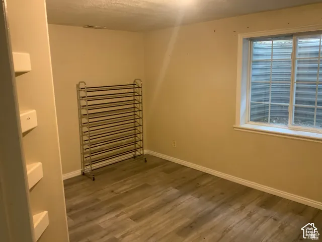 Room featuring wood-finish flooring, neutral-tone walls, and an egress-style window with a metal window well