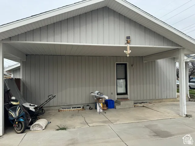 Covered carport featuring vertical siding, concrete flooring, and an exterior entryway with concrete steps