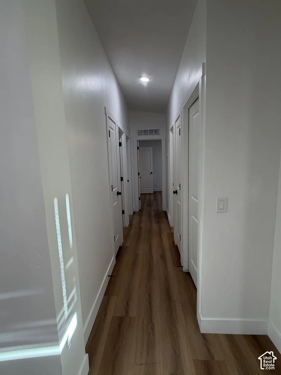 Hallway featuring wood-finish flooring, recessed lighting, and multiple interior paneled doors with matte black hardware