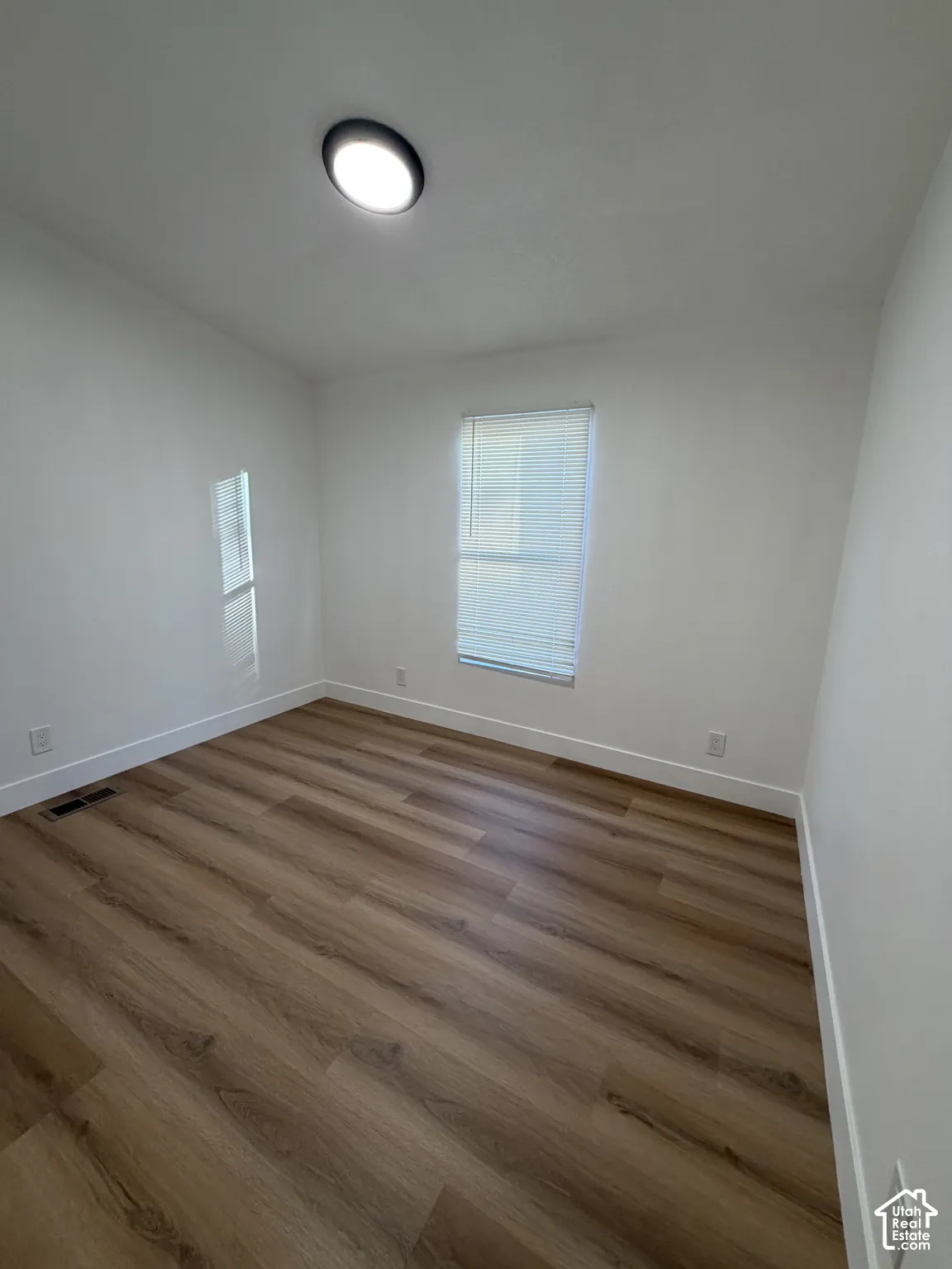 Room featuring wood-finish flooring, neutral walls, a single window with blinds, and a flush-mount ceiling light fixture