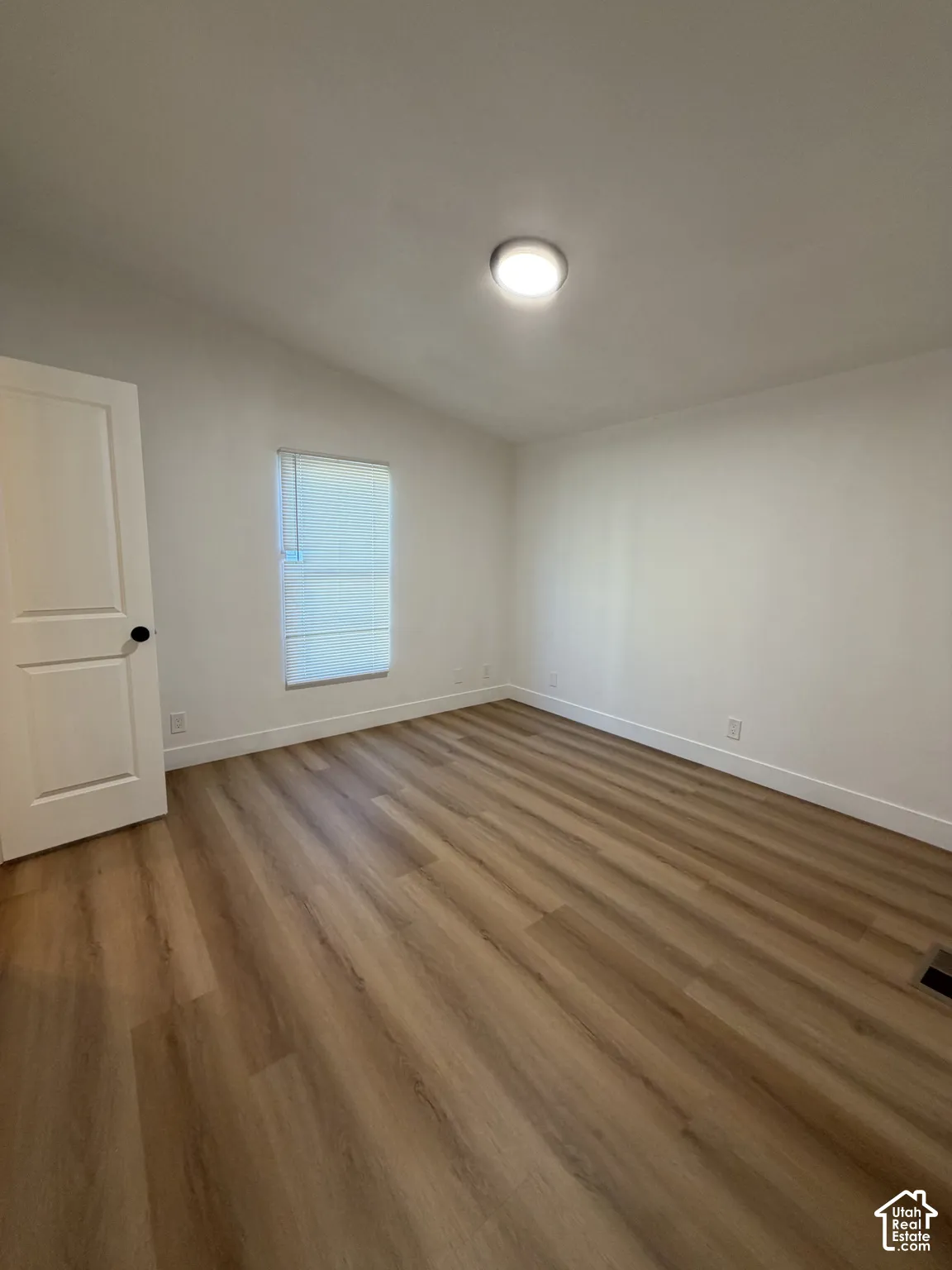 Neutral wall paint, wood-finish flooring, recessed ceiling lighting, and a single-panel interior door