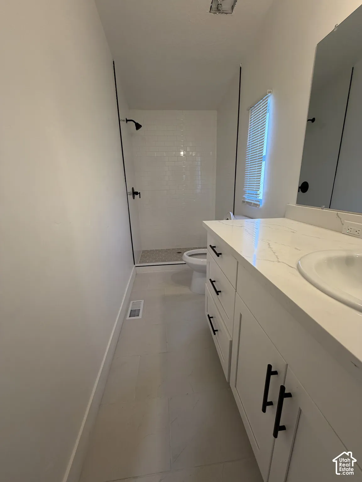White vanity cabinet with light-toned solid surface countertop, matte black hardware, subway tile shower surround, and neutral tile flooring