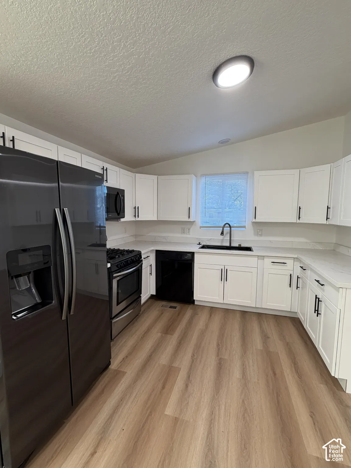 Kitchen featuring shaker-style white cabinetry, stone-surface countertops, wood-finish flooring, a dark-toned dual-basin sink with a gooseneck faucet, and stainless steel appliances