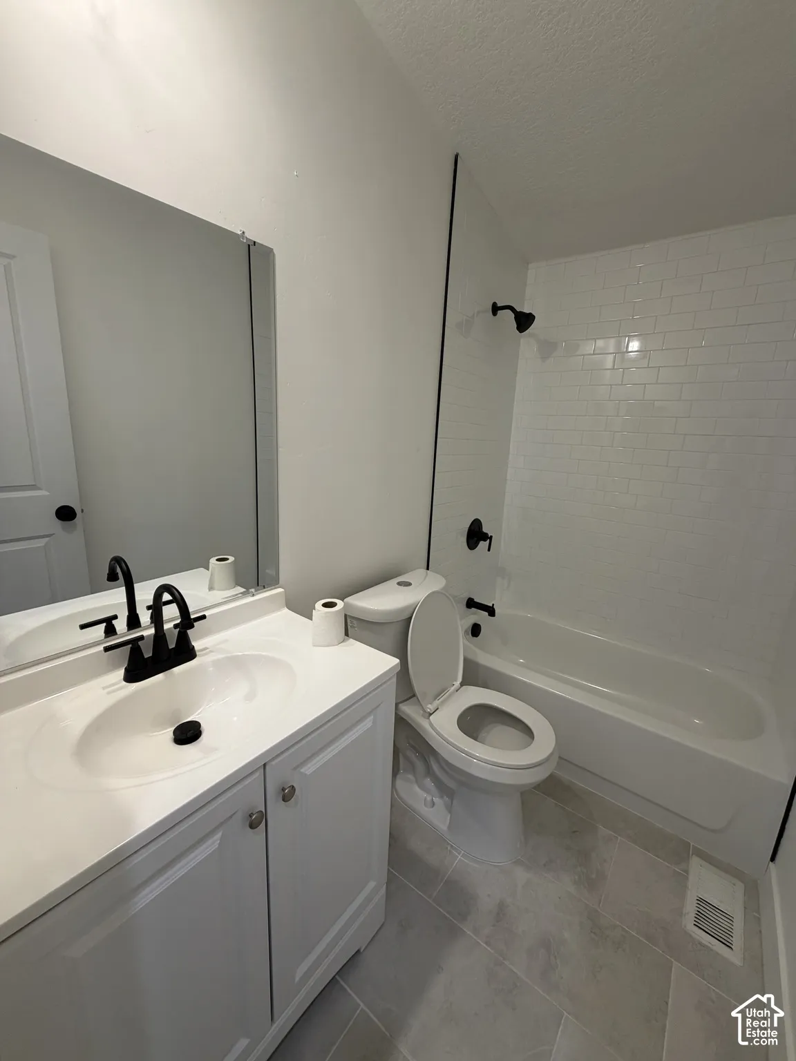 Bathroom featuring a white vanity cabinet, rectangular mirror, tub with white subway tile surround, matte black hardware, and tile flooring