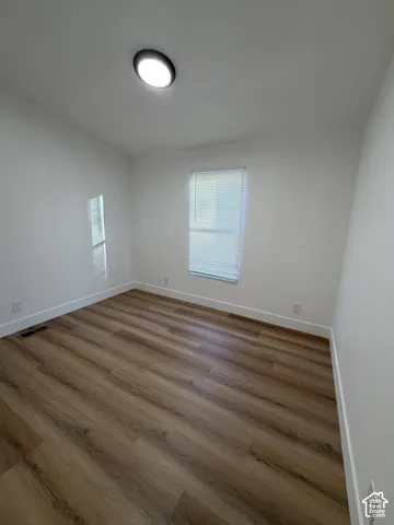 Room featuring wood-finish flooring, neutral walls, a single window with blinds, and a flush-mount ceiling light fixture