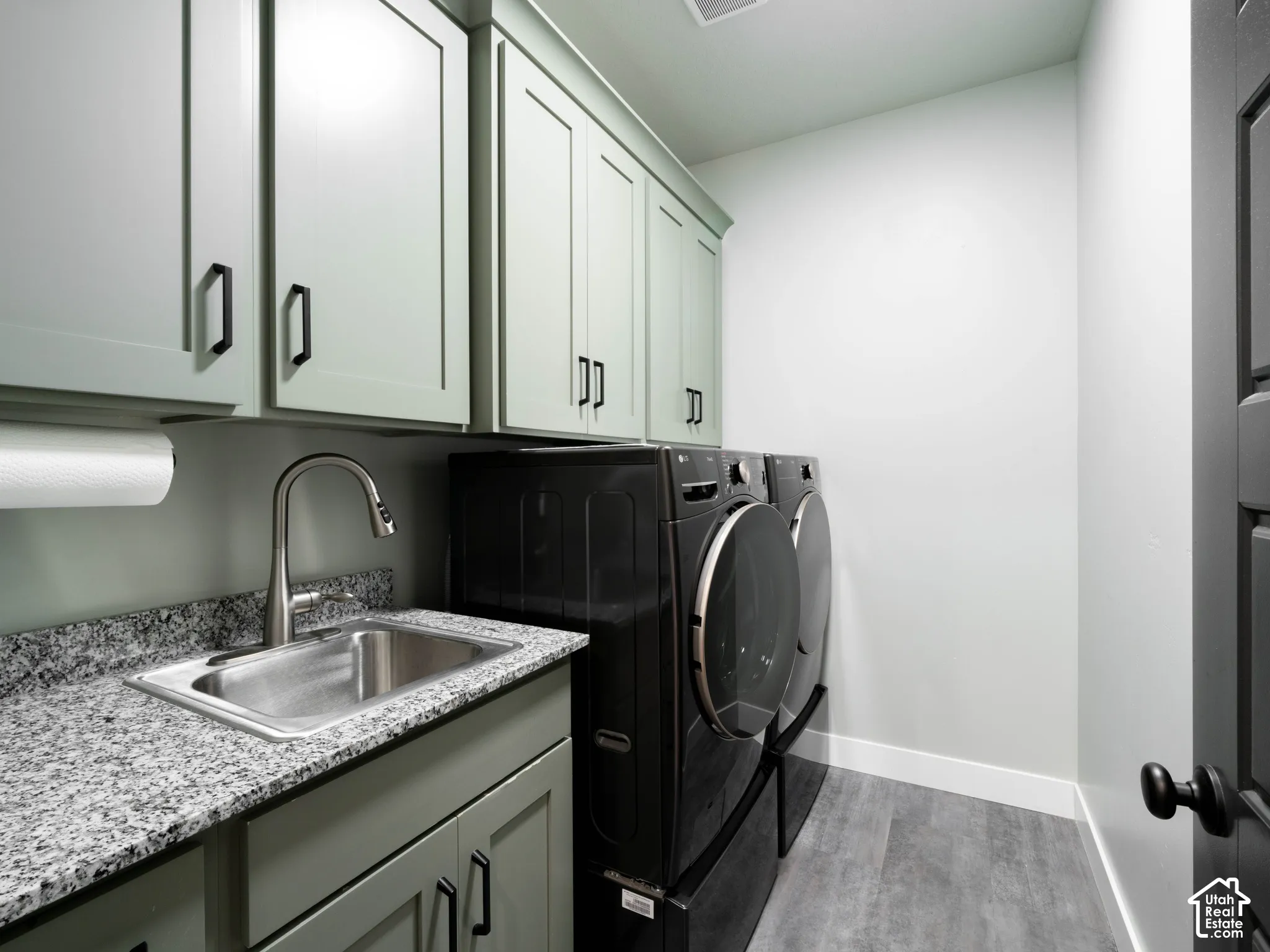 Laundry room featuring light green cabinetry, granite-style countertop with an undermount sink, and wood-finish flooring