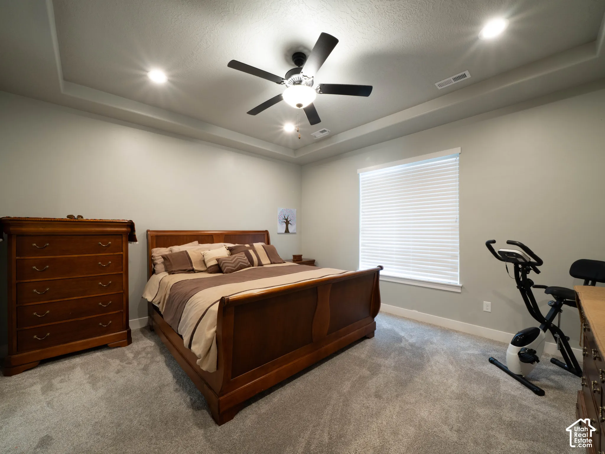 Primary bedroom. Tray ceiling with recessed lighting and a ceiling fan, light-toned wall paint, and window with blinds