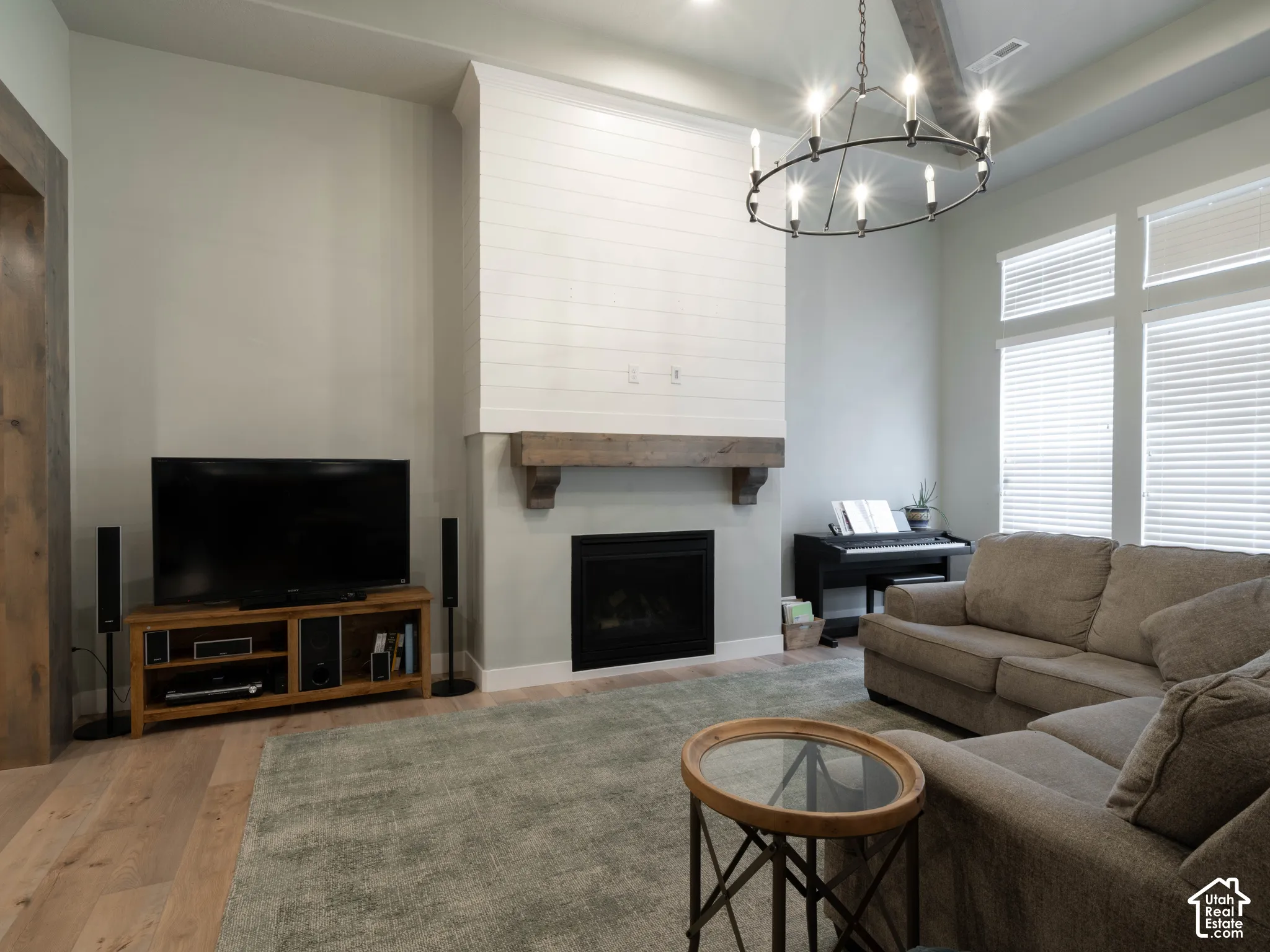 Vaulted ceiling with an exposed beam, wood-finish flooring, fireplace with a substantial wood mantel, and multiple large windows
