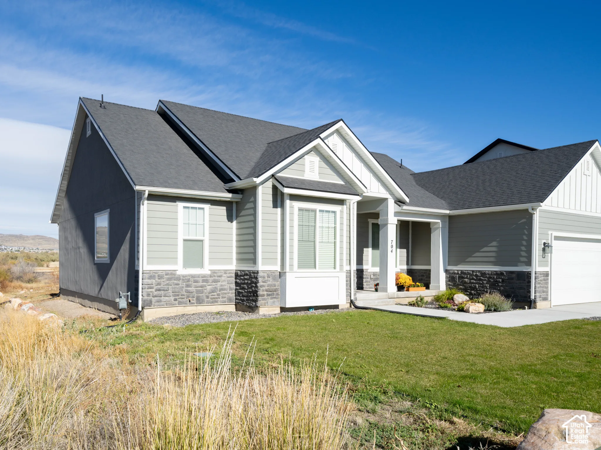 Contemporary exterior featuring gray siding, stone-finish accents, a dark shingle roof, a bay window, and an attached garage