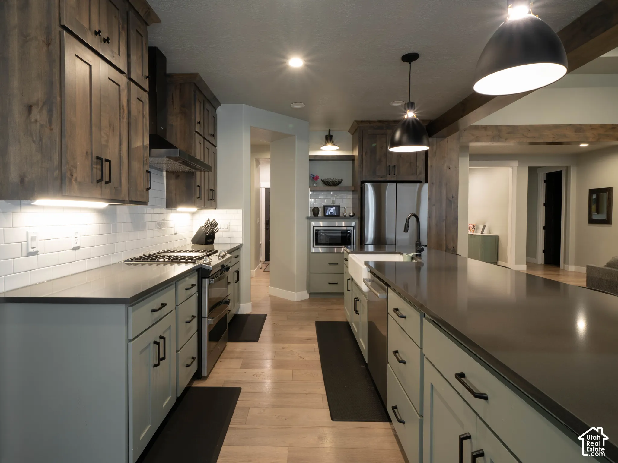 Kitchen featuring wood-finish flooring, dark wood upper cabinetry, light grey lower cabinetry, stainless steel appliances, and dark countertops