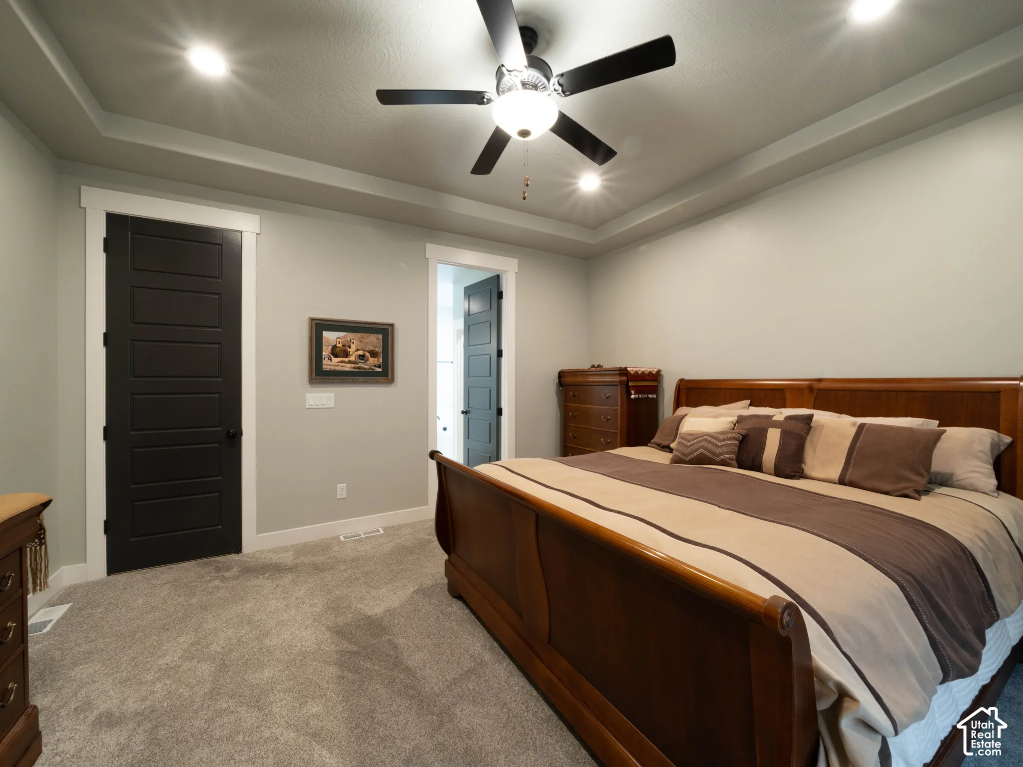 Primary bedroom. Tray ceiling with recessed lighting, ceiling fan, grey carpeting, and dark paneled doors with white trim