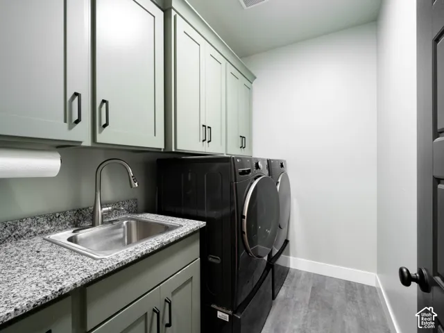 Laundry room featuring light green cabinetry, granite-style countertop with an undermount sink, and wood-finish flooring