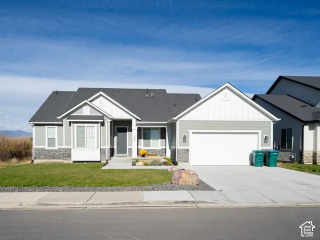 Modern construction exterior featuring light gray siding, dark gray roof, stone veneer accents, and a two-car garage. No neighbors on one side, behind, or across from due to protected land.