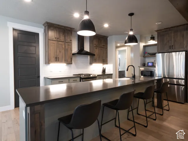 Kitchen featuring wood-finish flooring, a large island with countertop seating, stainless steel appliances, dark wood cabinetry, and a subway tile backsplash