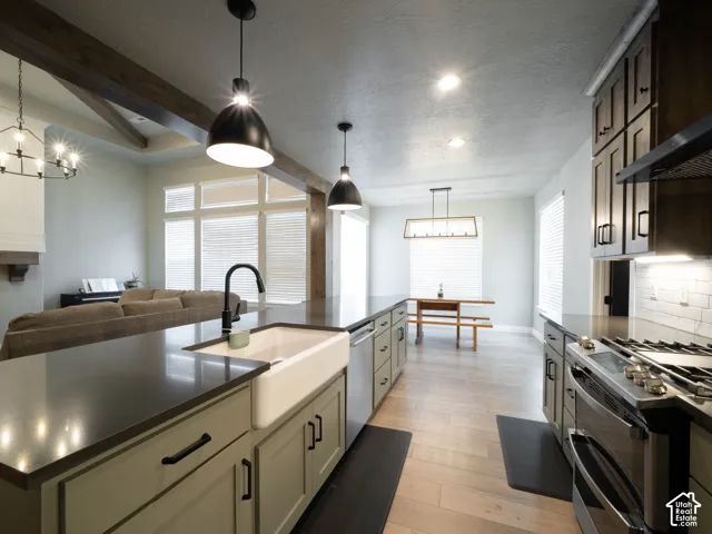 Kitchen featuring light green cabinetry, dark countertops, a white farmhouse sink, and stainless steel appliances