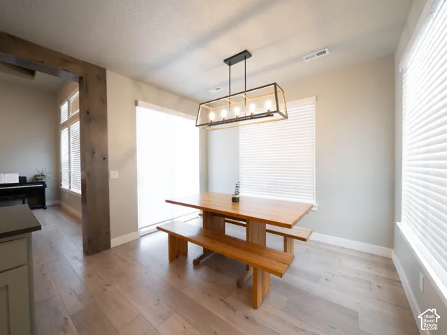 Light wood-finish flooring with a modern linear chandelier and white window blinds