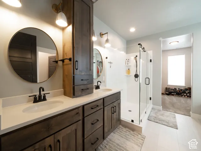Primary ensuite bathroom. Double vanity with white countertops, wood-finish cabinetry, and matte black fixtures. Large walk-in closet