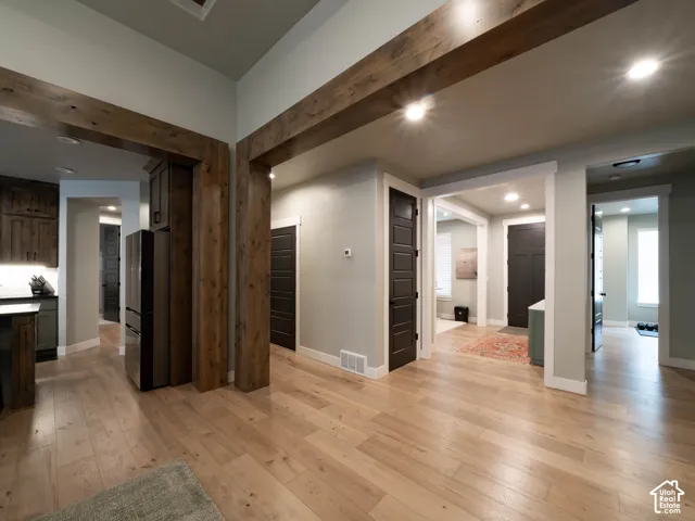 Exposed wood beams, recessed lighting, light wood-finish flooring, dark wood cabinetry, and dark panel doors