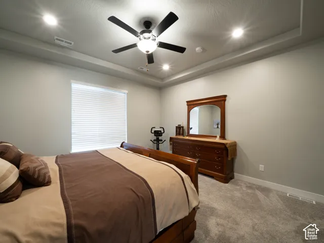 Primary bedroom. Tray ceiling with recessed lighting and a ceiling fan, window with blinds, and neutral wall tones