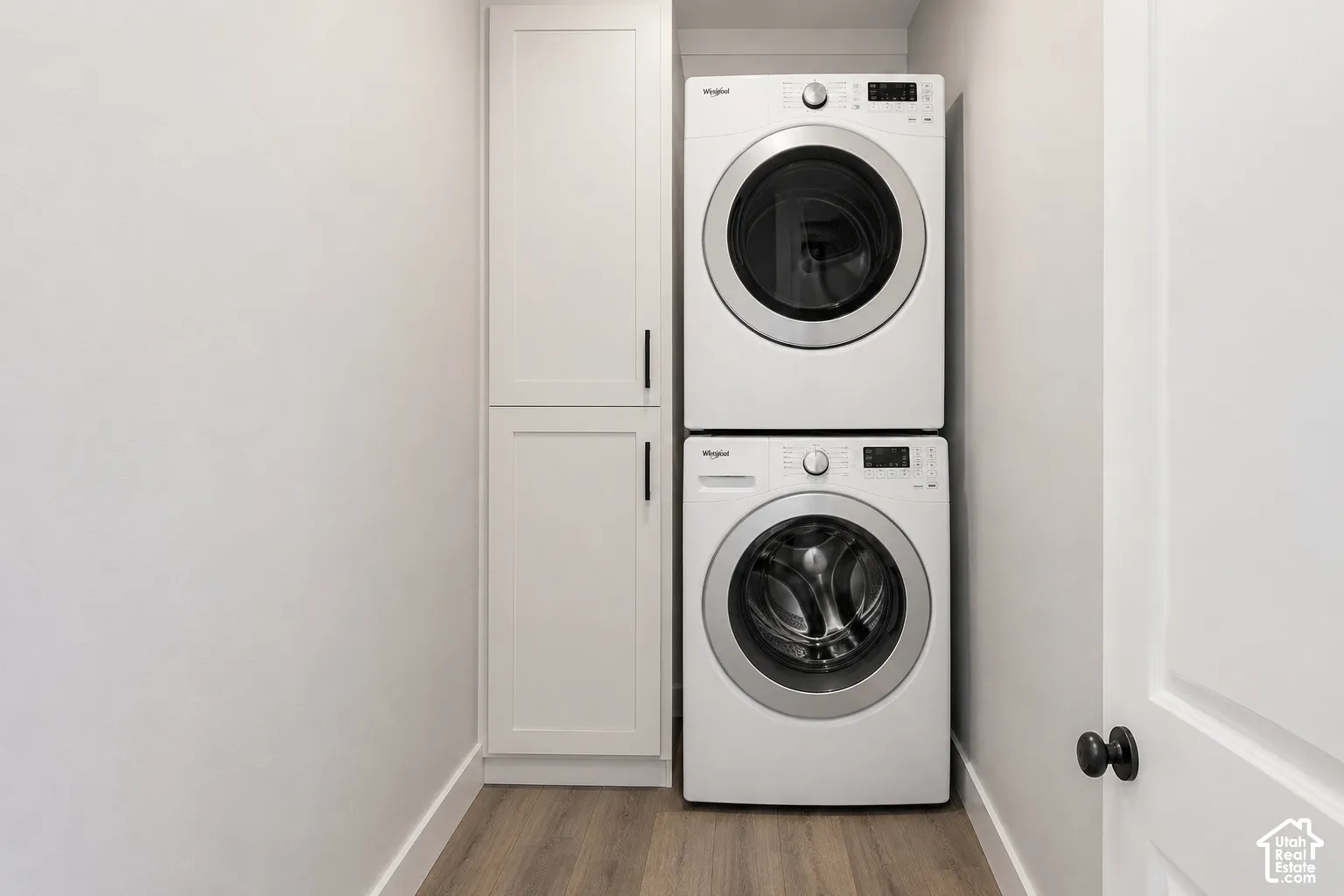 Laundry area featuring stacked appliances and floor-to-ceiling built-in cabinetry with matte black hardware, finished with wood-finish flooring
