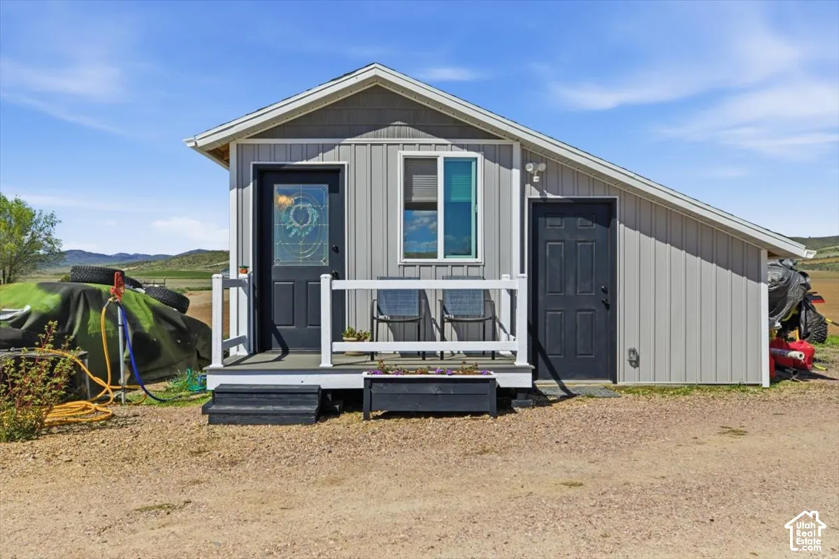 Exterior featuring vertical panel siding, a front porch with white railing, a glass-inset entry door, and a single-slope roofline