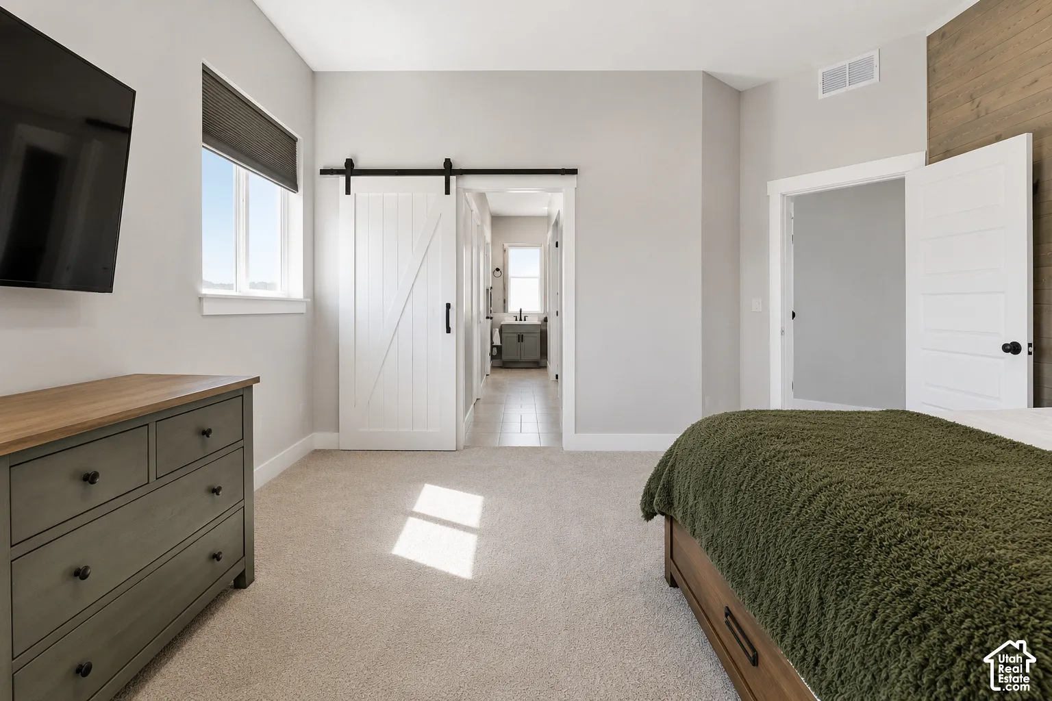 Bedroom featuring a wood-finish accent wall, sliding barn door with matte black hardware, neutral carpeting, and a window with a roller shade