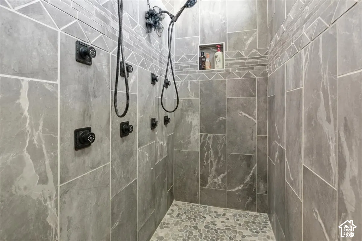 Walk-in shower featuring floor-to-ceiling stone-finish tile, dual shower heads, multiple wall-mounted body sprays, pebble-stone flooring, and a recessed tiled niche