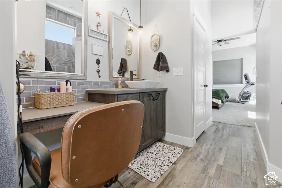 Vanity area featuring wood-finish cabinetry, a rectangular vessel sink, gray subway tile backsplash, framed wall mirror, and wood-finish flooring