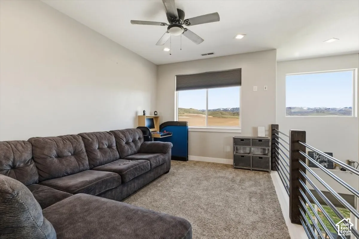 Spacious room featuring neutral carpeting, a ceiling fan with integrated lighting, recessed lighting, and a metal horizontal-bar railing
