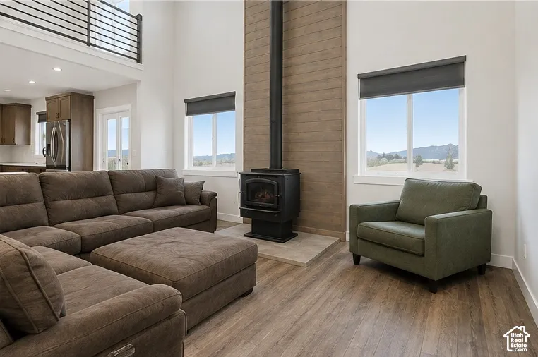 Vaulted ceilings featuring a metal loft railing, wood-finish flooring, wood-paneled accent wall, and a black freestanding fireplace on a tiled hearth