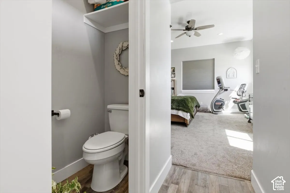 Enclosed water closet featuring wood-finish flooring, a white toilet, and a built-in overhead storage shelf