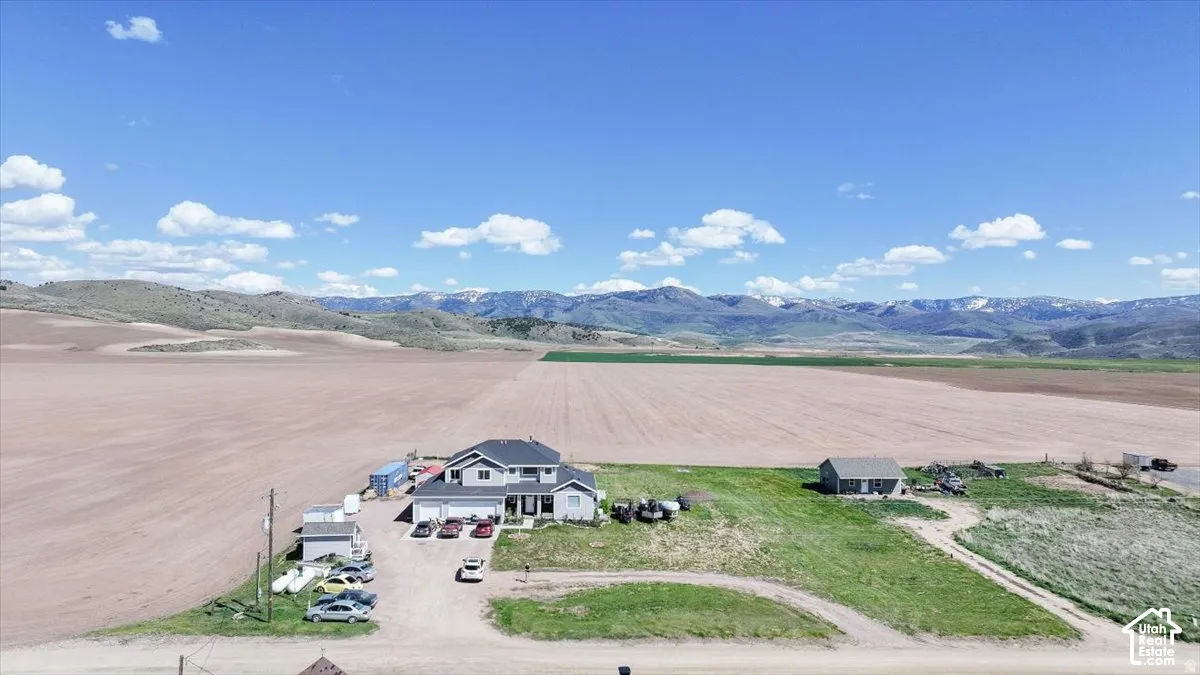 Two-story residence featuring a multi-car garage, secondary detached structure, expansive acreage, and mountain range backdrop