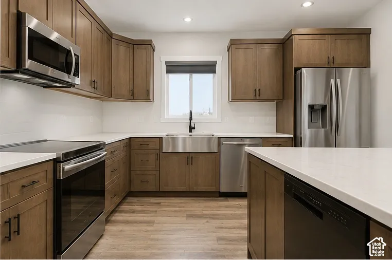Kitchen featuring wood-finish cabinetry, stainless steel appliances, white countertops, an apron-front sink with a matte black faucet, and wood-finish flooring