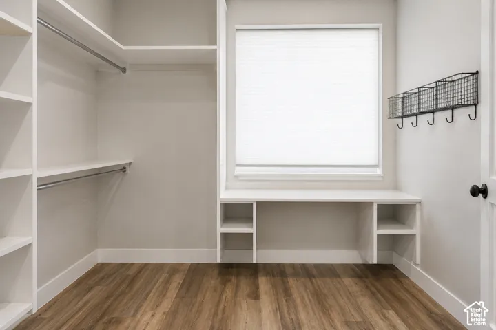 Custom walk-in closet featuring white built-in shelving, dual hanging rods, a central workstation with lower cubbies, and wood-finish flooring