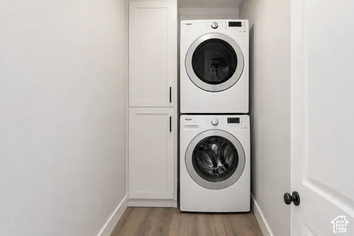 Laundry area featuring stacked appliances and floor-to-ceiling built-in cabinetry with matte black hardware, finished with wood-finish flooring