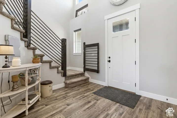 Entryway featuring high ceilings, wood-finish flooring, a white paneled door with a glass insert, and a staircase with horizontal metal balusters