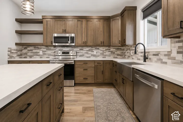 Kitchen featuring wood-finish cabinetry, solid surface countertops, a stainless steel farmhouse sink, open shelving, and a multi-tone tile backsplash