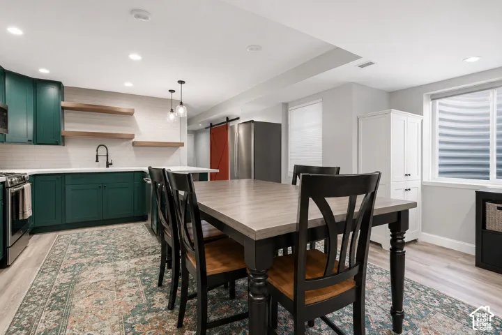 Kitchen featuring dark teal cabinetry, white subway tile backsplash, floating wood-finish shelves, matte black faucet, and a sliding red barn-style door