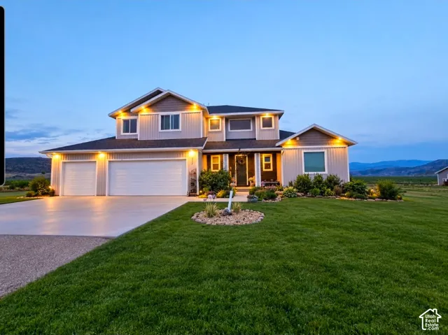 Two-story residence featuring vertical and horizontal siding, a three-car garage, concrete driveway, and expansive lawn with manicured landscaping